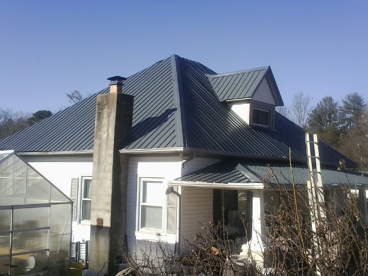 Dark blue standing seam metal roof on a white farmhouse with dormer — Slate & Tile Roof Repair by Roofing Brothers in Lost Nation