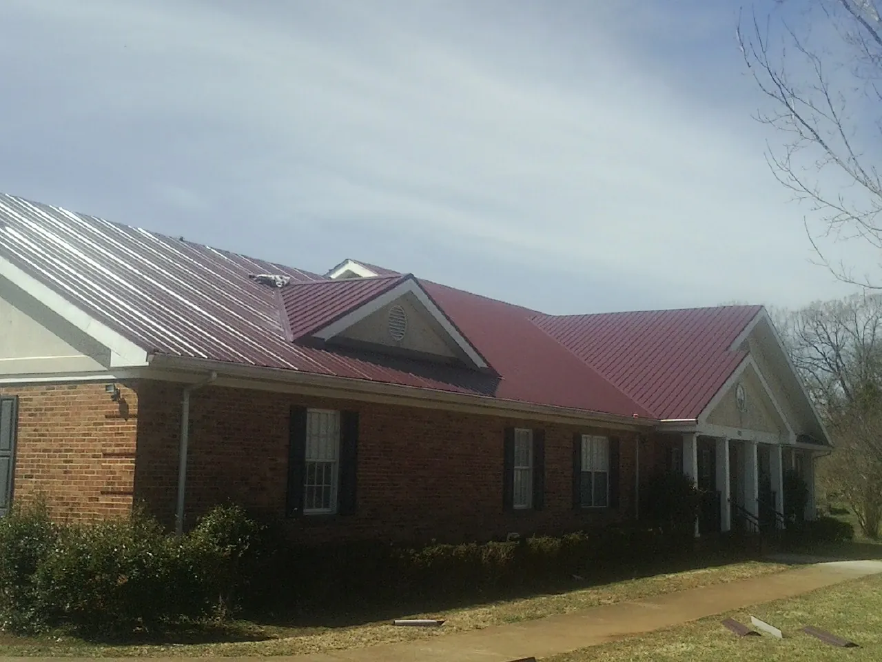 Red metal roof with gabled entries on a long brick building, from a Hail Damage Roof Repair job in Lost Nation