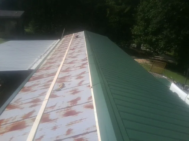 Old rusted panels beside newly installed green metal roofing — Wind Damage Roof Repair by Roofing Brothers in Lost Nation