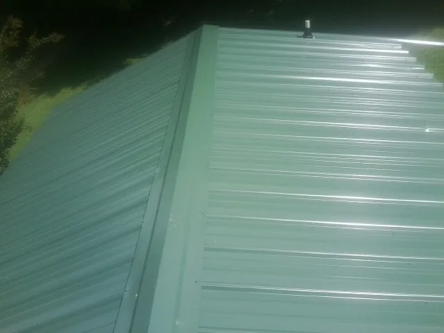 New green metal panels meeting at the ridge of a roof — Flat Roof Repair work by our crew in Lost Nation