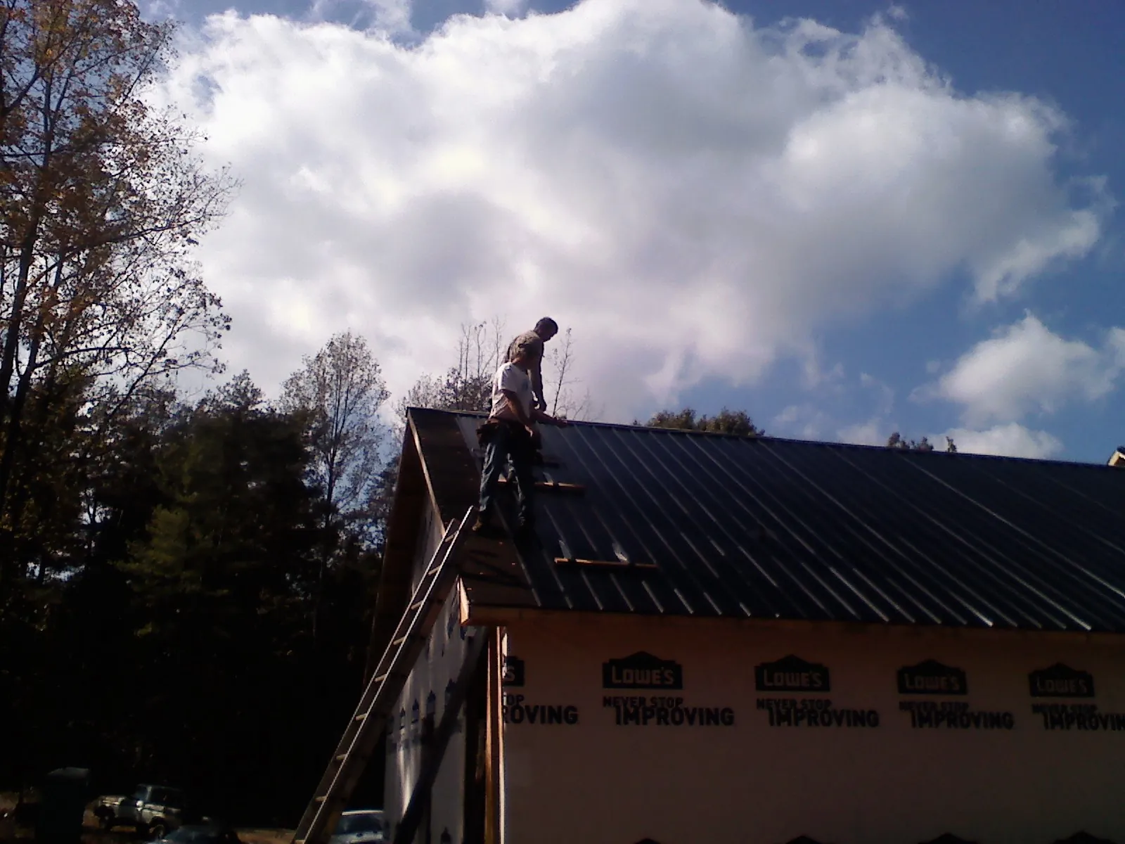Roofer fastening dark metal panels high against a cloudy sky, from a Roof Inspection job in Lost Nation