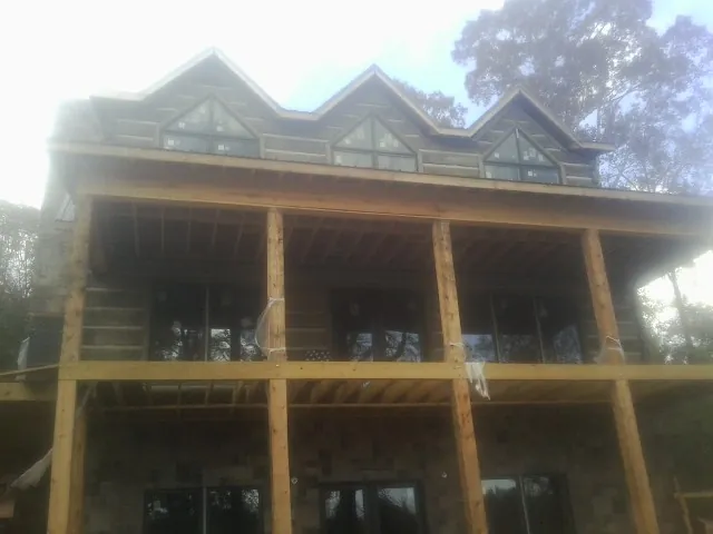 Dormers and porch framing on a large log home under construction — Roof Coating work by our crew in Lost Nation