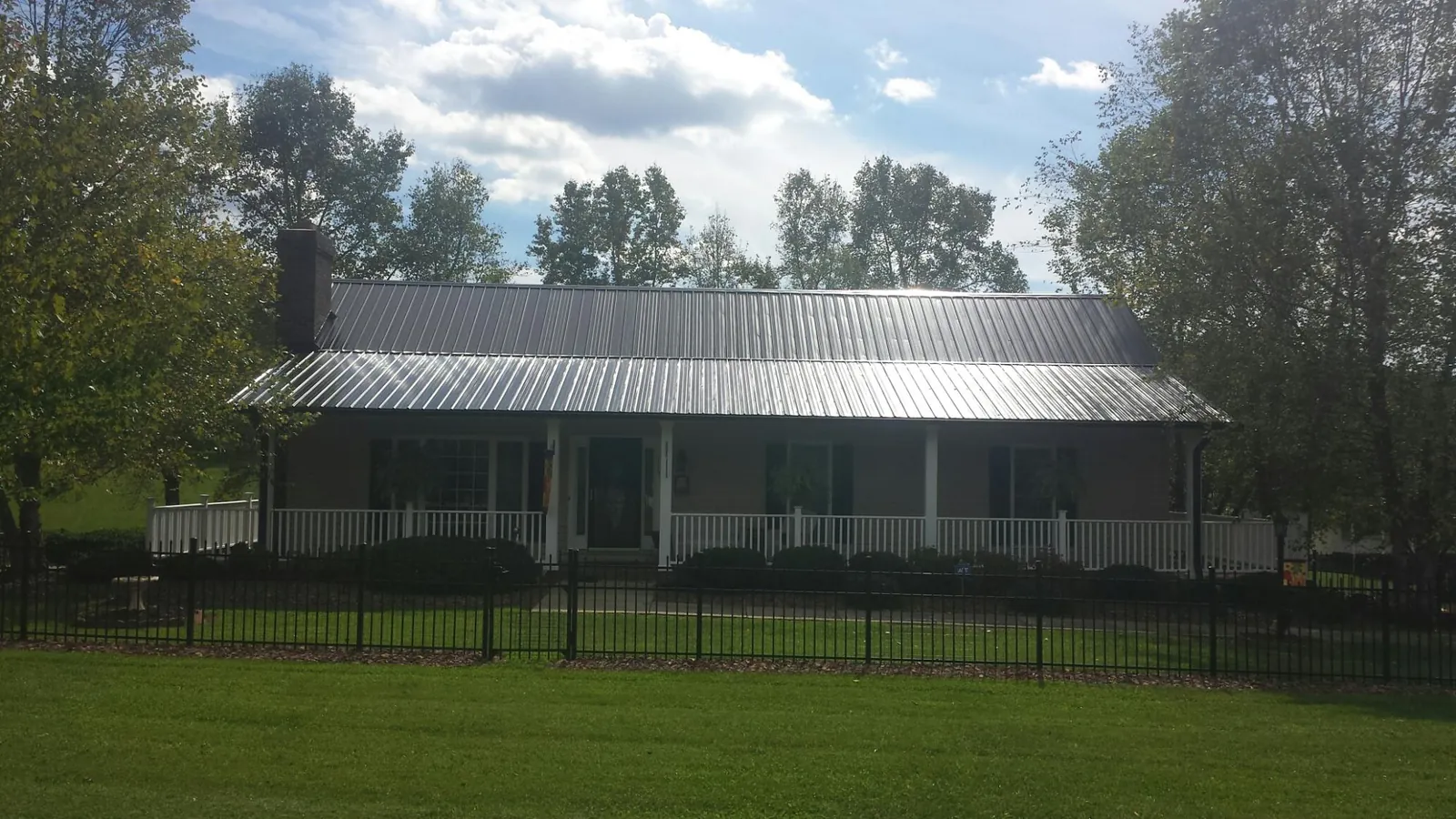 Gray metal roof on a brick ranch with a full width front porch — Gutter Guard Installation work by our crew in Lost Nation