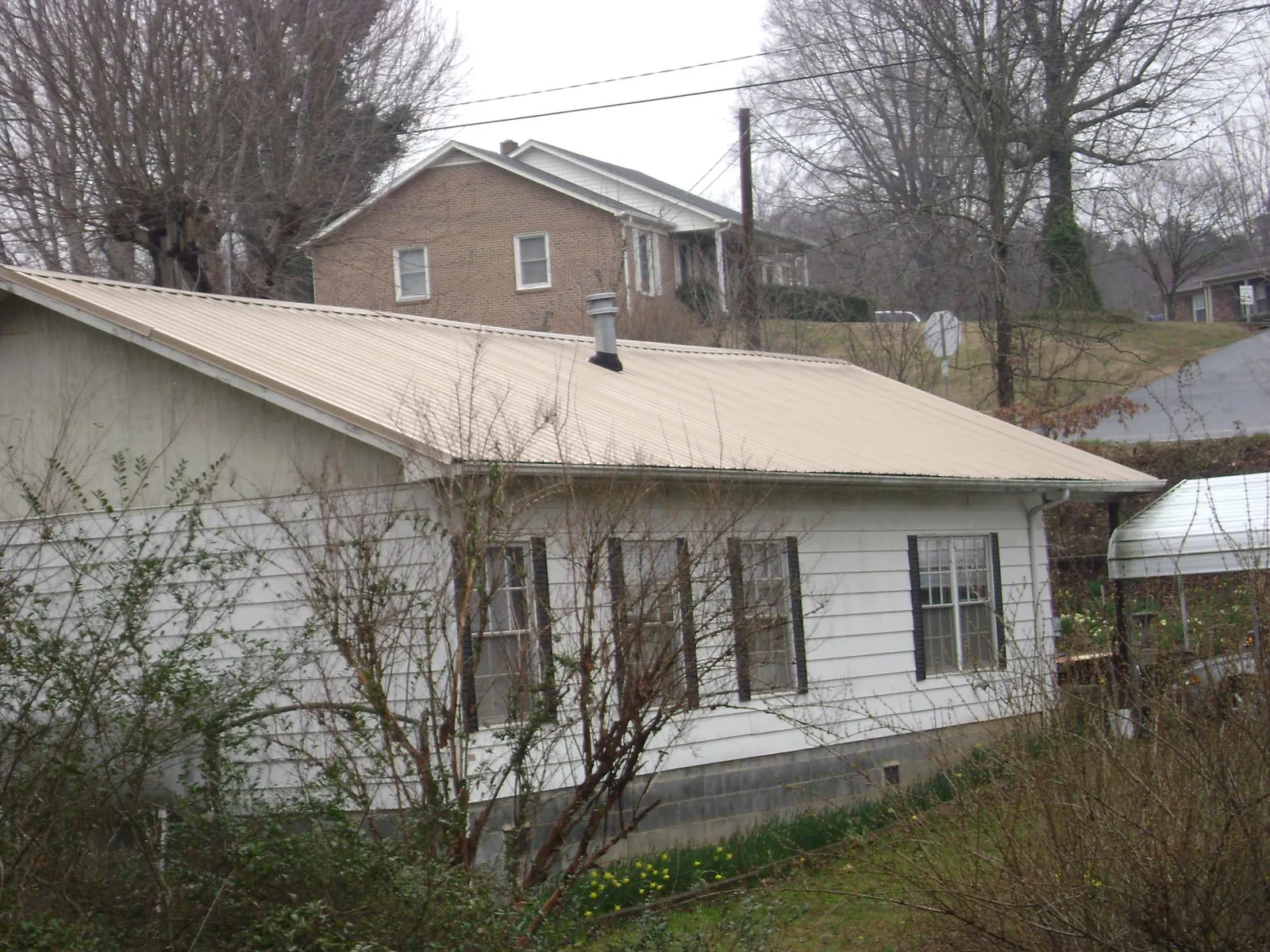 Tan metal roof on a white sided house set into a hillside — Commercial Roofing by Roofing Brothers in Lost Nation