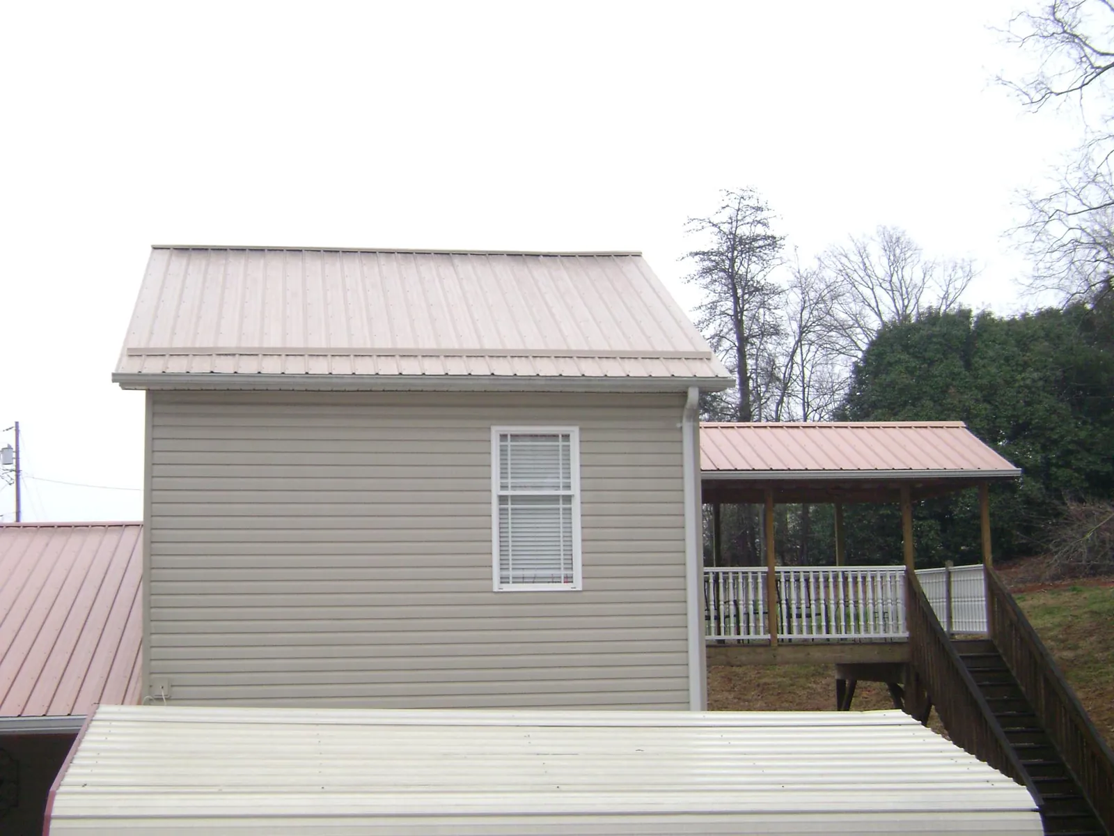 Tan metal roofs on a two story addition and attached porch, from a Roof Replacement job in Lost Nation